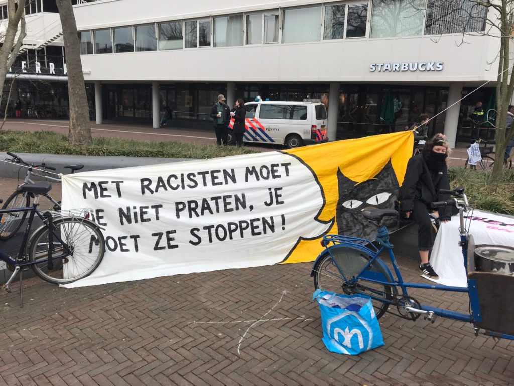 Een spandoek met een zwarte kat en een tekstballon waar in staat "Met racisten moet je niet praten, je moet ze stoppen!".