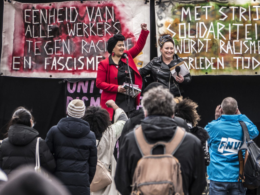 Nassima el Idrissi staat met haar vuist in de lucht op het podium, met naast haar de persoon met wie ze zojuist een gedicht heeft voorgedragen.