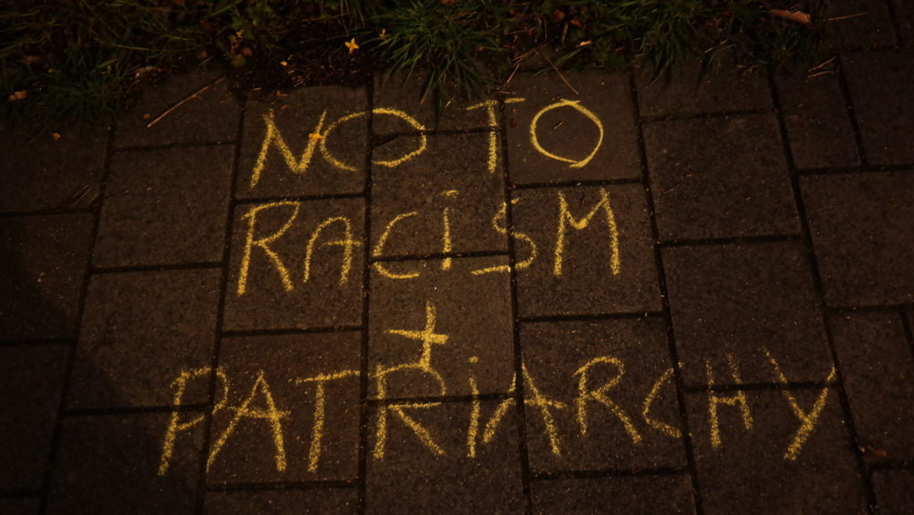 Krijttekst op straat: "No to racism + patriarchy"