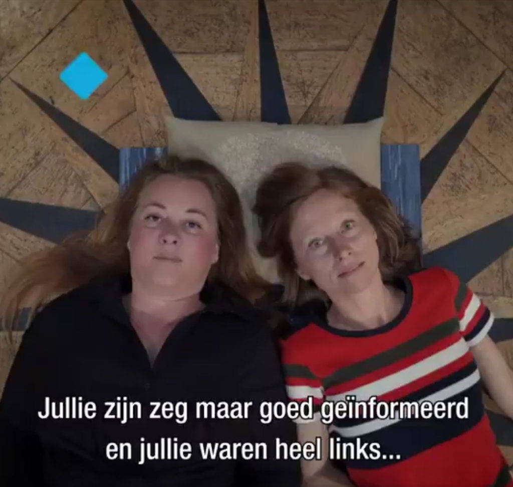 Screen capture uit de documentaire Samenzwevers van Sunny Bergman. Twee mensen liggen op hun rug op de grond en ze kijken in de camera. Beide hebben lang haar. De één draagt een zwarte blouse, de ander een rood retrotruitje met brede strepen erop. Een stukje ondertiteling is zichtbaar: "Jullie zijn zeg maar goed geïnormeerd en jullie waren heel links...".