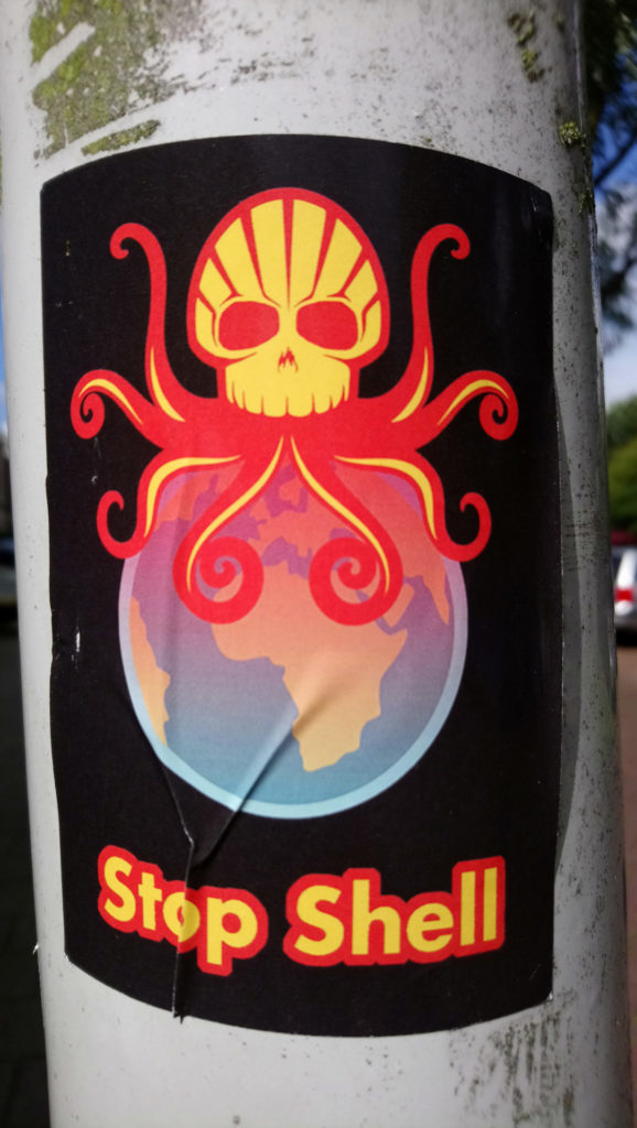 Sticker waarop het logo van Shell onderdeel is van een octopus met doodshoofd waarvan de tentakels de aarde omvatten.