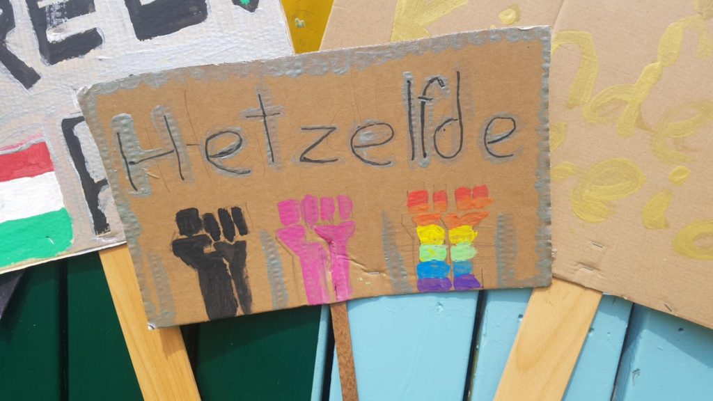 Een bord met de tekst "Hetzelfde" met daaronder geheven vuistjes in verschillende kleuren.