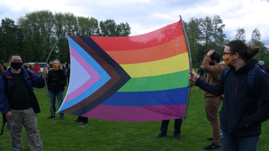 Enkele deelnemers houden een regenboogvlag vast voor de camera.