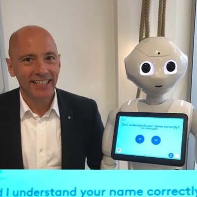 Ton Wilthagen naast een vriendelijk uitziende mensachtige robot met een tablet waar op staat "Did I understand your name correctly?".