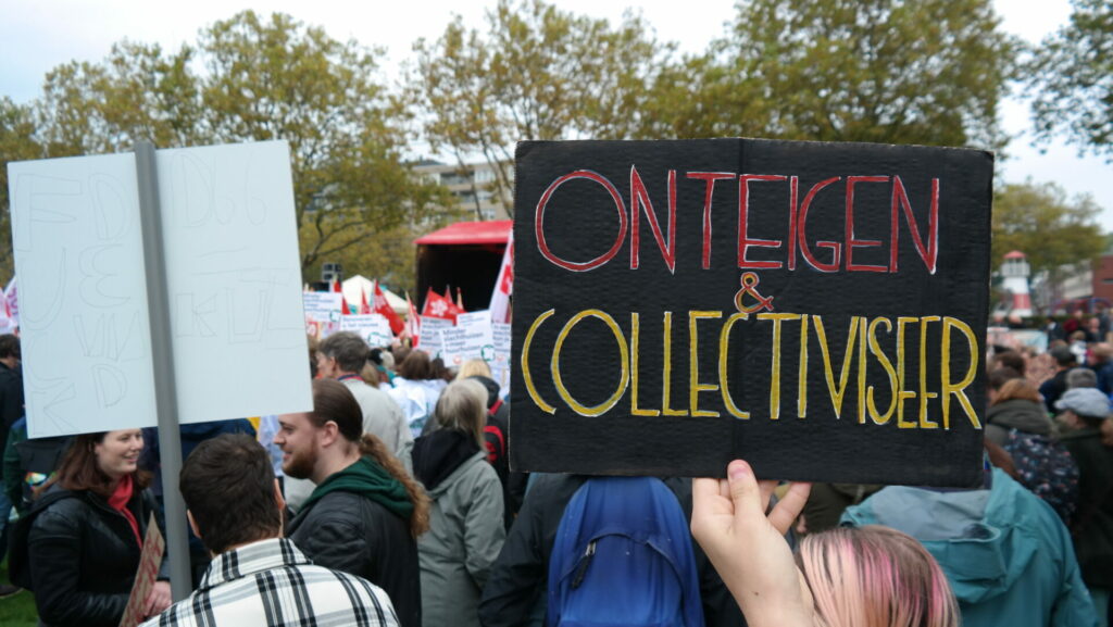 Een groep demonstranten op de Woonopstand in Rotterdam. Iemand draagt een bordje met de tekst 'onteigen & collectiviseer'.